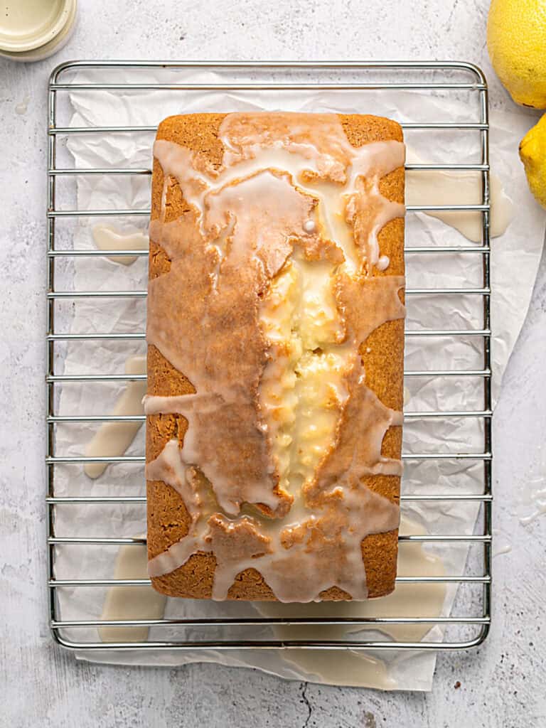 Glazing a lemon loaf cake on a wire rack with parchment paper below.
