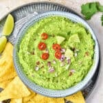 Guacamole with jalapeños in a blue bowl on a metal tray with tortilla chips.