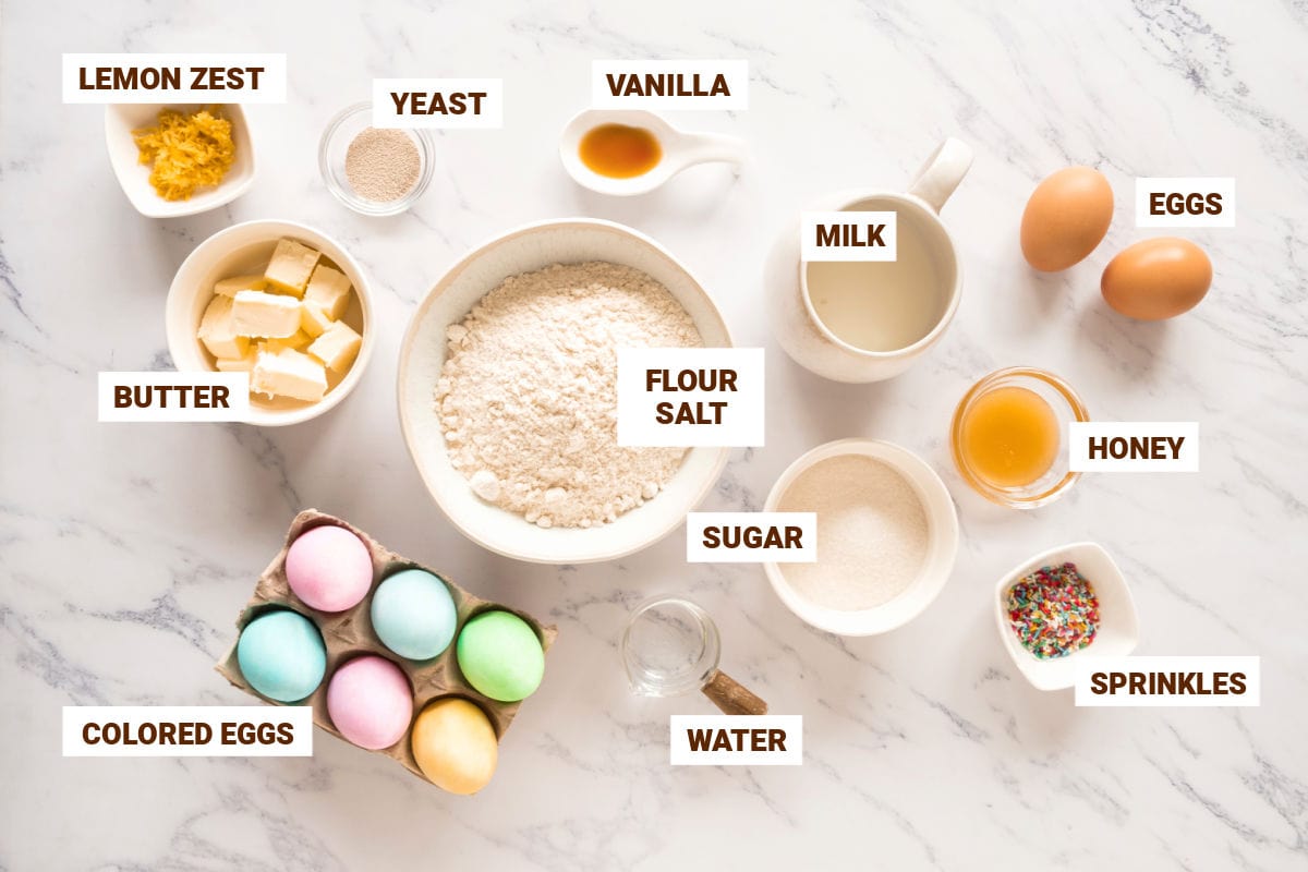 White bowls with ingredients for sweet bread with colored eggs. White marbled surface.