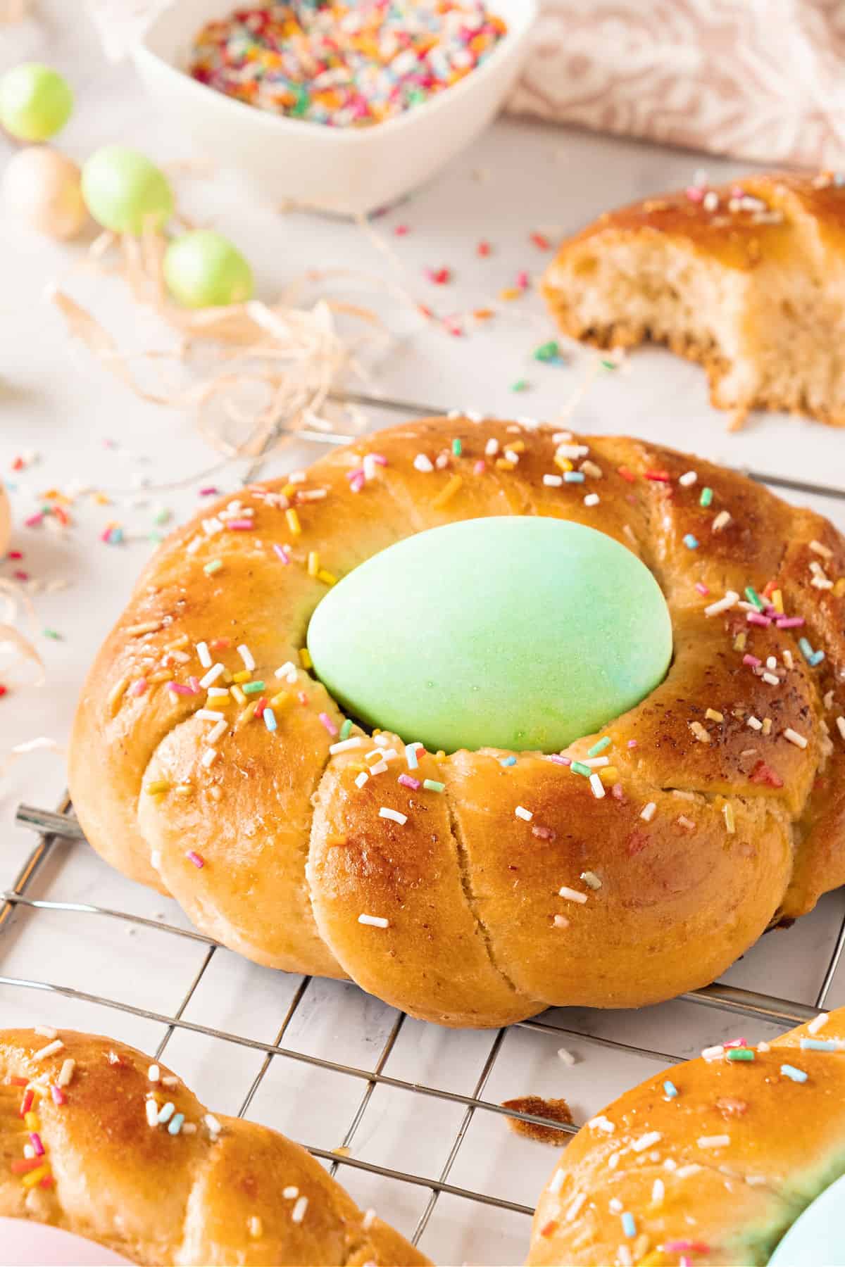 Easter braid with green egg and sprinkles on a wire rack. White background, bowl with sprinkles.