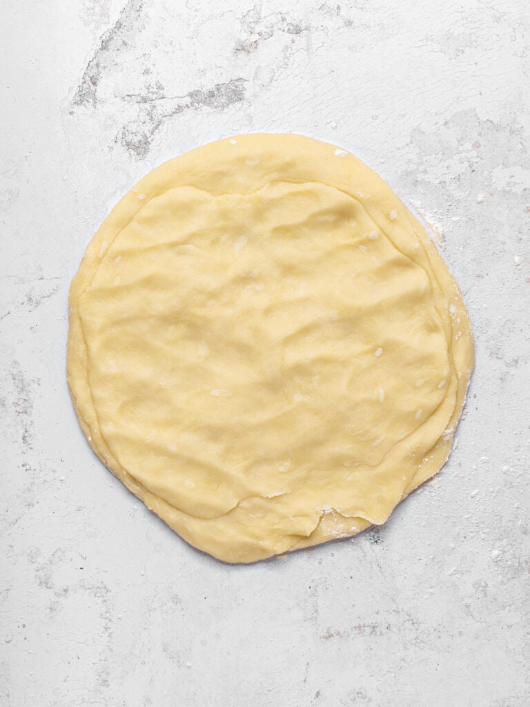 Layered pieces of rolled pie dough on a light gray surface.