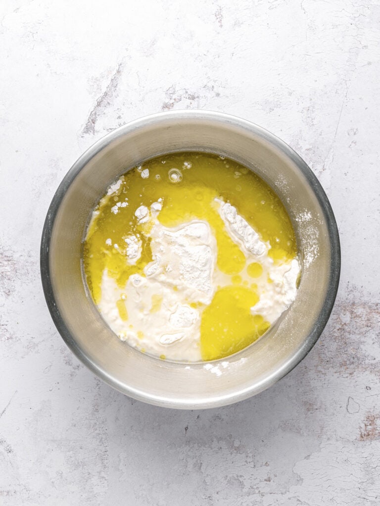 Metal bowl with flour mixture and olive oil. Light gray surface.