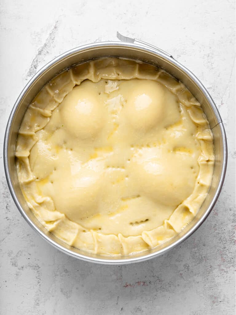 Double crusted pie in a round cake springform pan before baking. Light gray background.