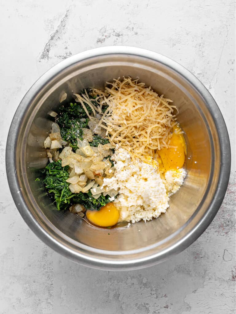 Metal bowl with ricotta, grated cheese, eggs and spinach. Top view. Light gray surface.