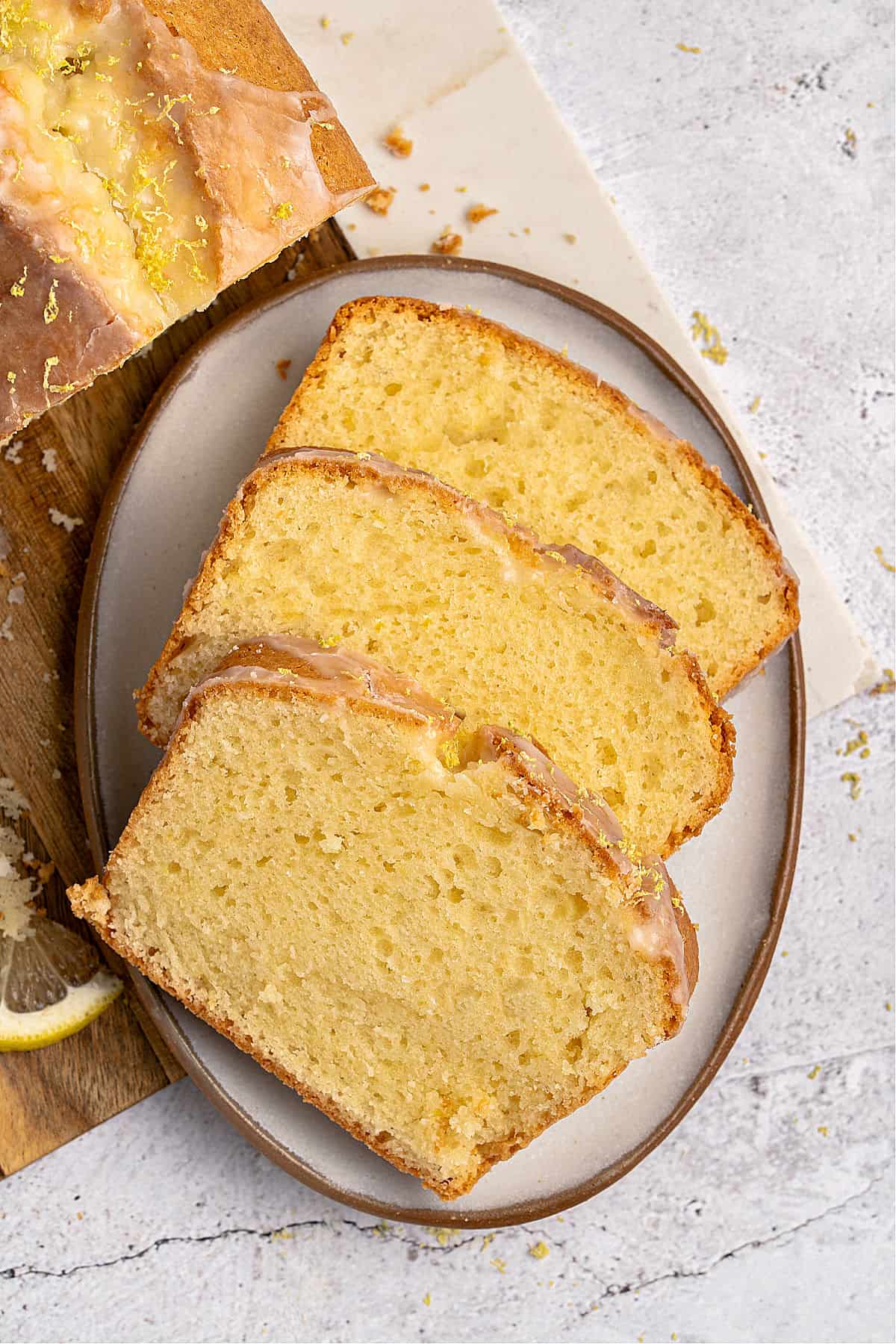 Three sliced of limoncello pound cake on a brown rimmed plate. Light gray background.