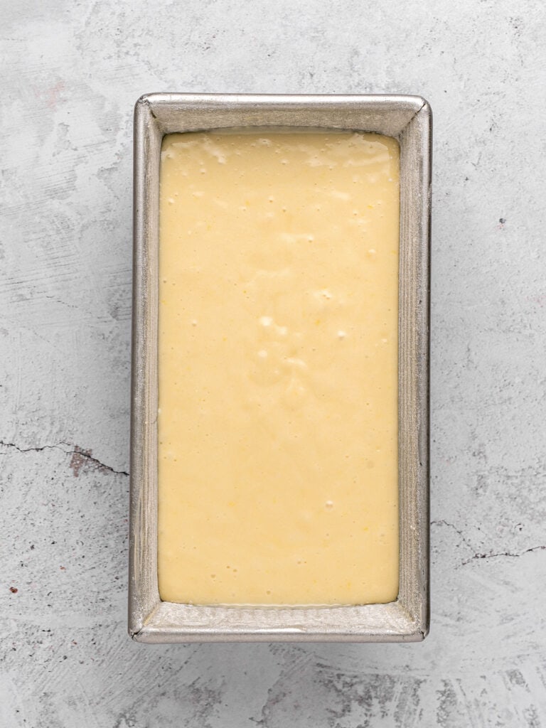 Loaf metal cake pan with lemon batter. Light gray surface, top view.
