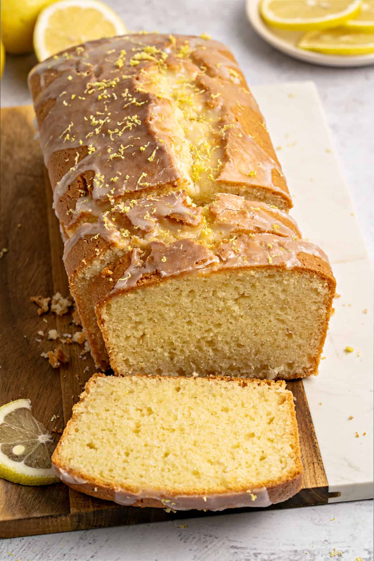 Loaf lemon cake with glaze on a wooden board. Light gray background, lemon slices.