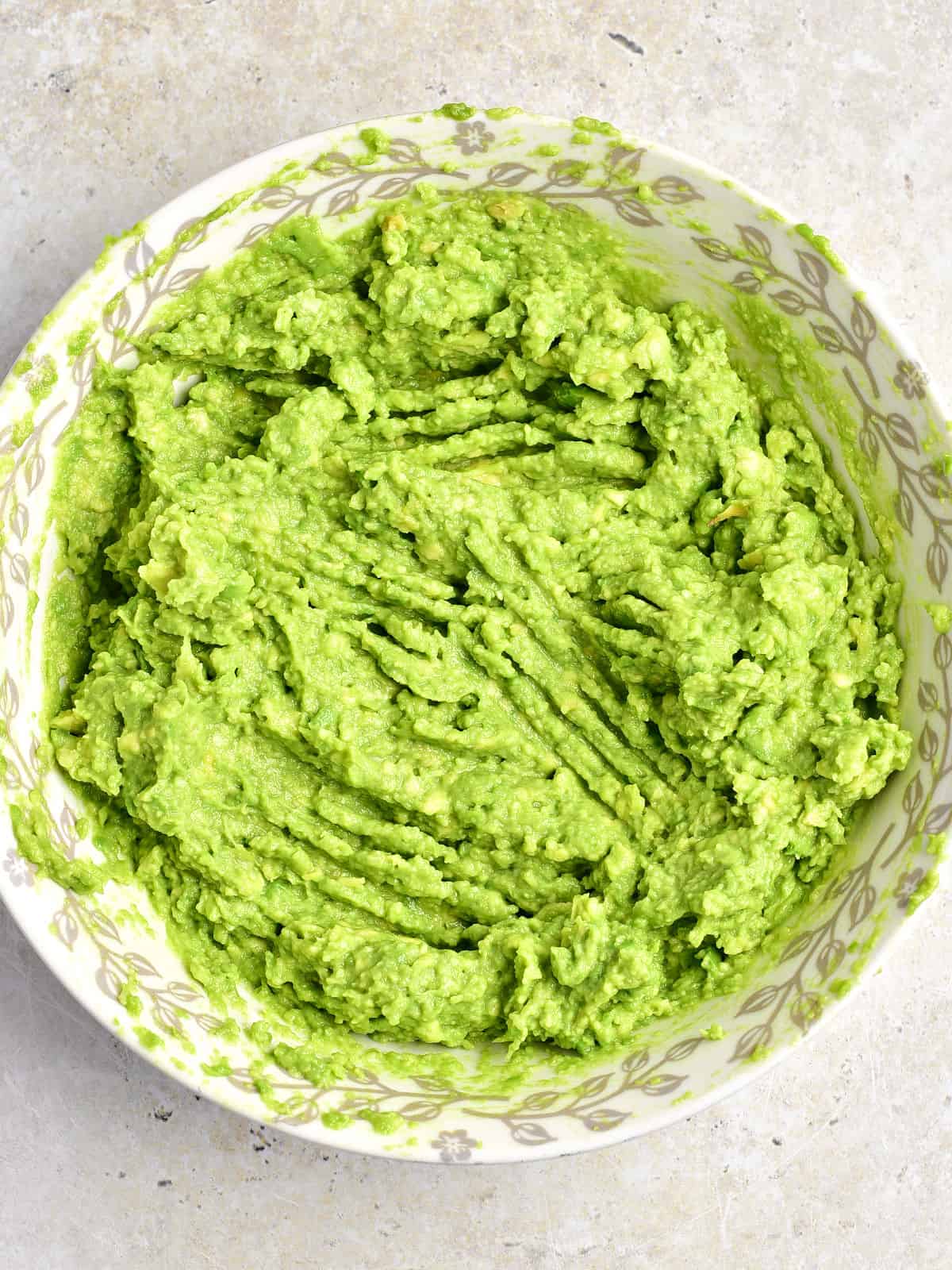 White bowl of mashed avocados. Light gray background.