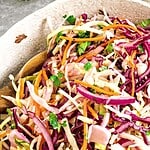 Green, red and white text overlay on coleslaw in a white bowl.