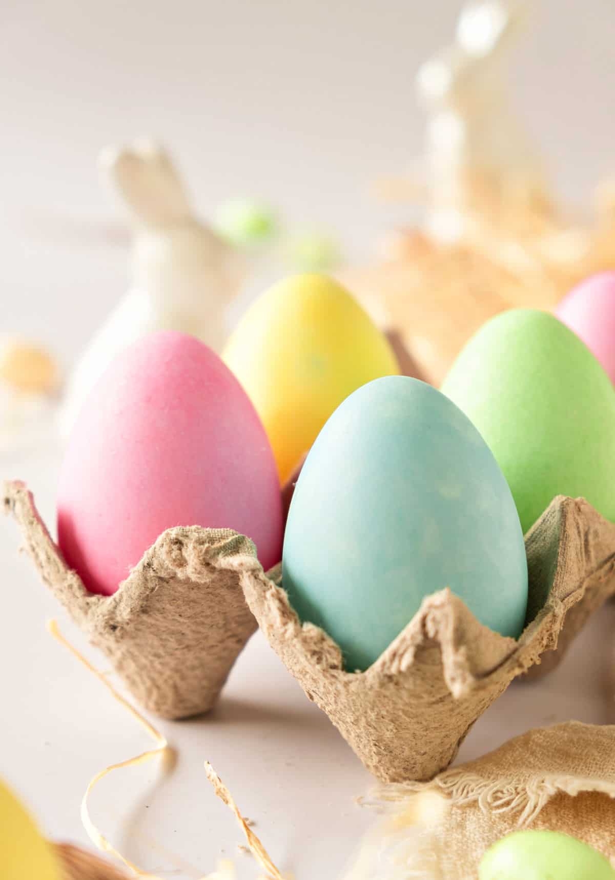 Beige egg cartoon with colored eggs. Ceramic bunnies on a white background.
