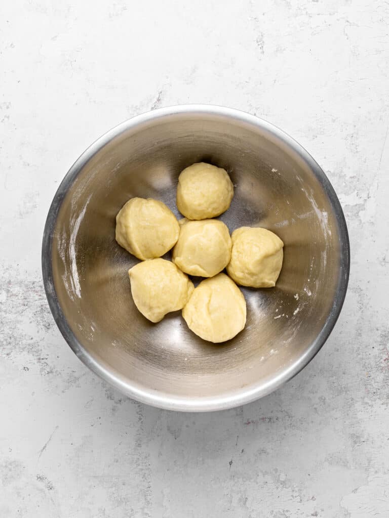 Six pieces of dough in a metal bowl. Light gray background. Top view.