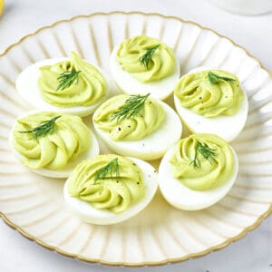White scalloped plate with avocado deviled eggs with dill.