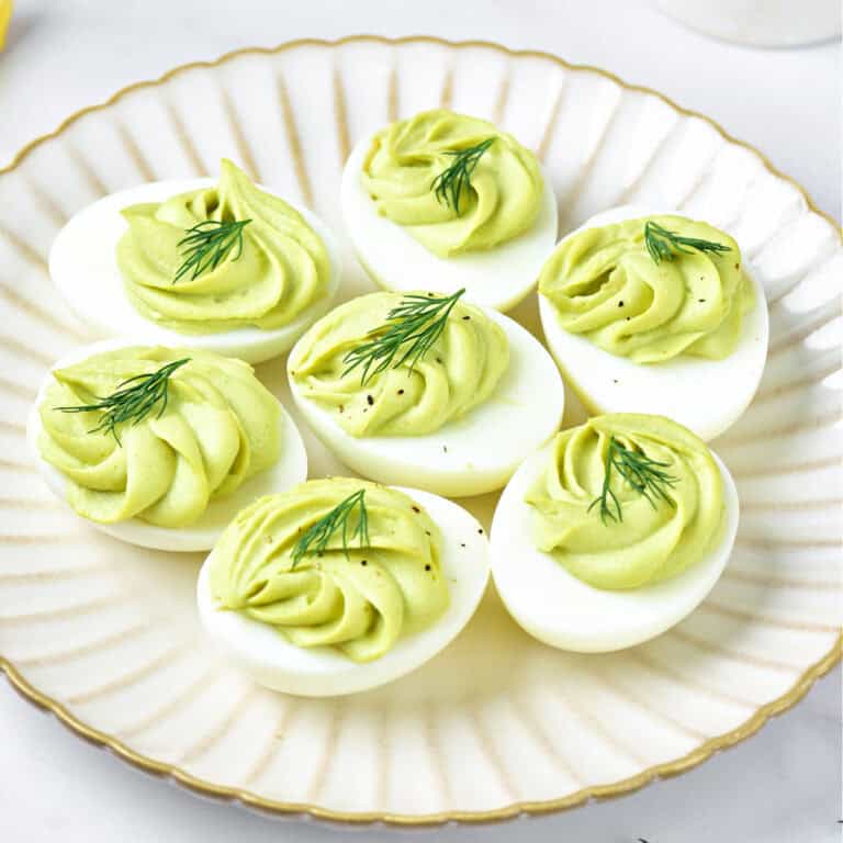 White scalloped plate with avocado deviled eggs with dill.