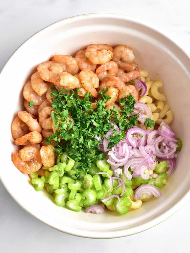 Shrimp, celery, shallots, parsley and pasta in a white bowl. Top view.