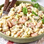 Pasta salad with shrimp on a green plate. Parsley leaves, wooden serving utensils.