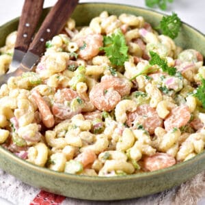 Pasta salad with shrimp on a green plate. Parsley leaves, wooden serving utensils.