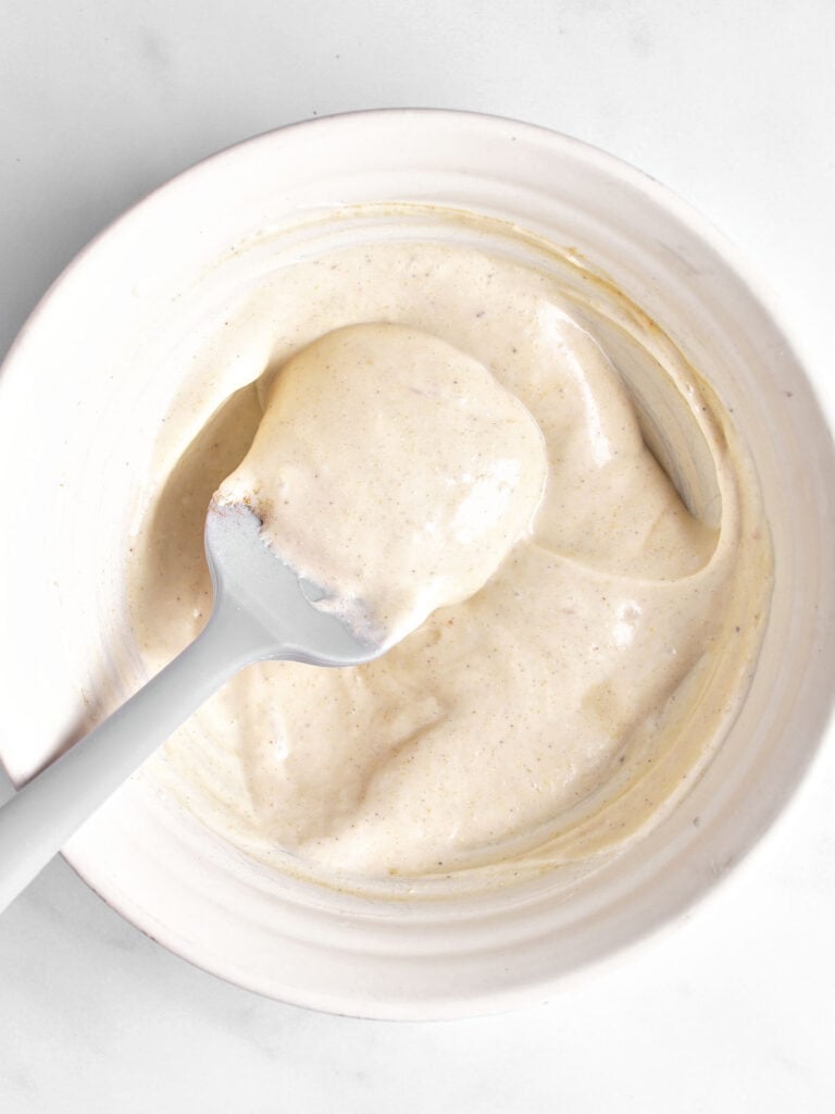 Mayo dressing for pasta salad in a white bowl. Gray spatula. White background.