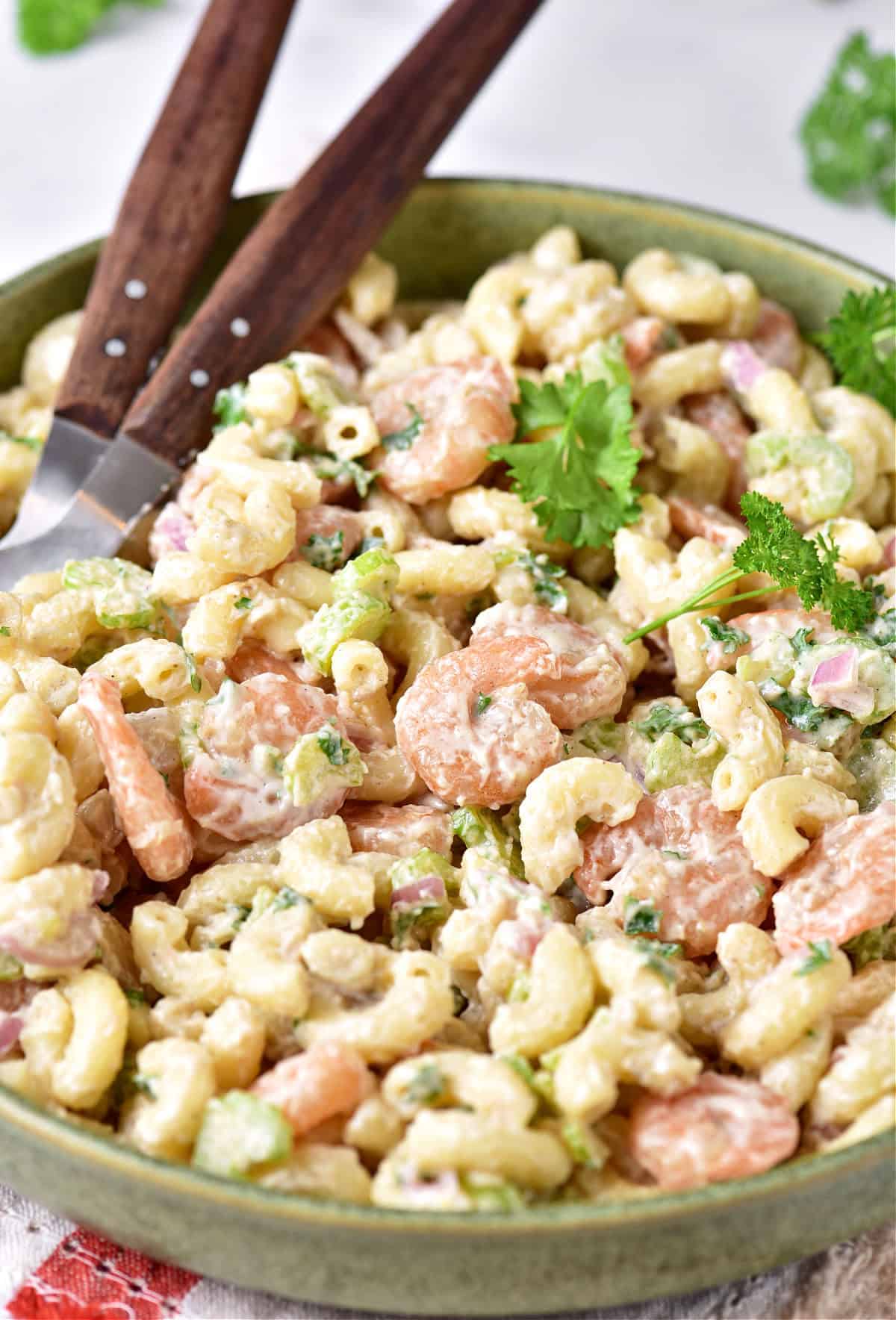 Shrimp pasta salad on a green plate with parsley leaves. Wooden serving spoons.