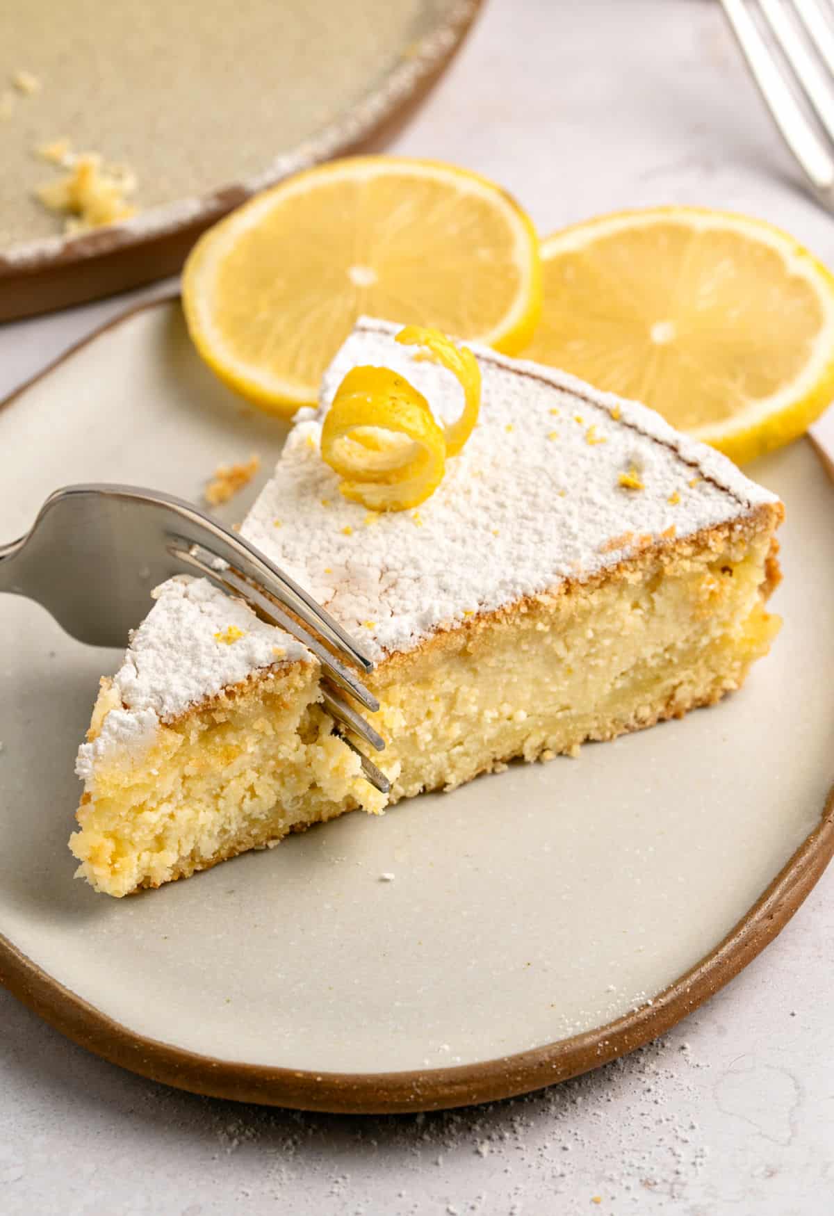 Forking into a lemo ricotta pie slice on a beige plate. Lemon slices.