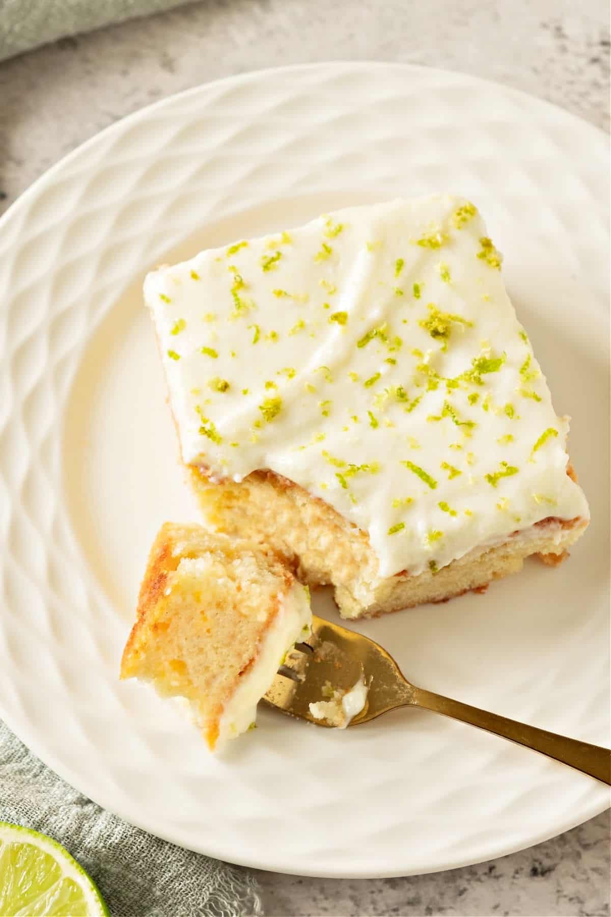 Forked bite of tequila cream cake with rest of slice on a white plate.