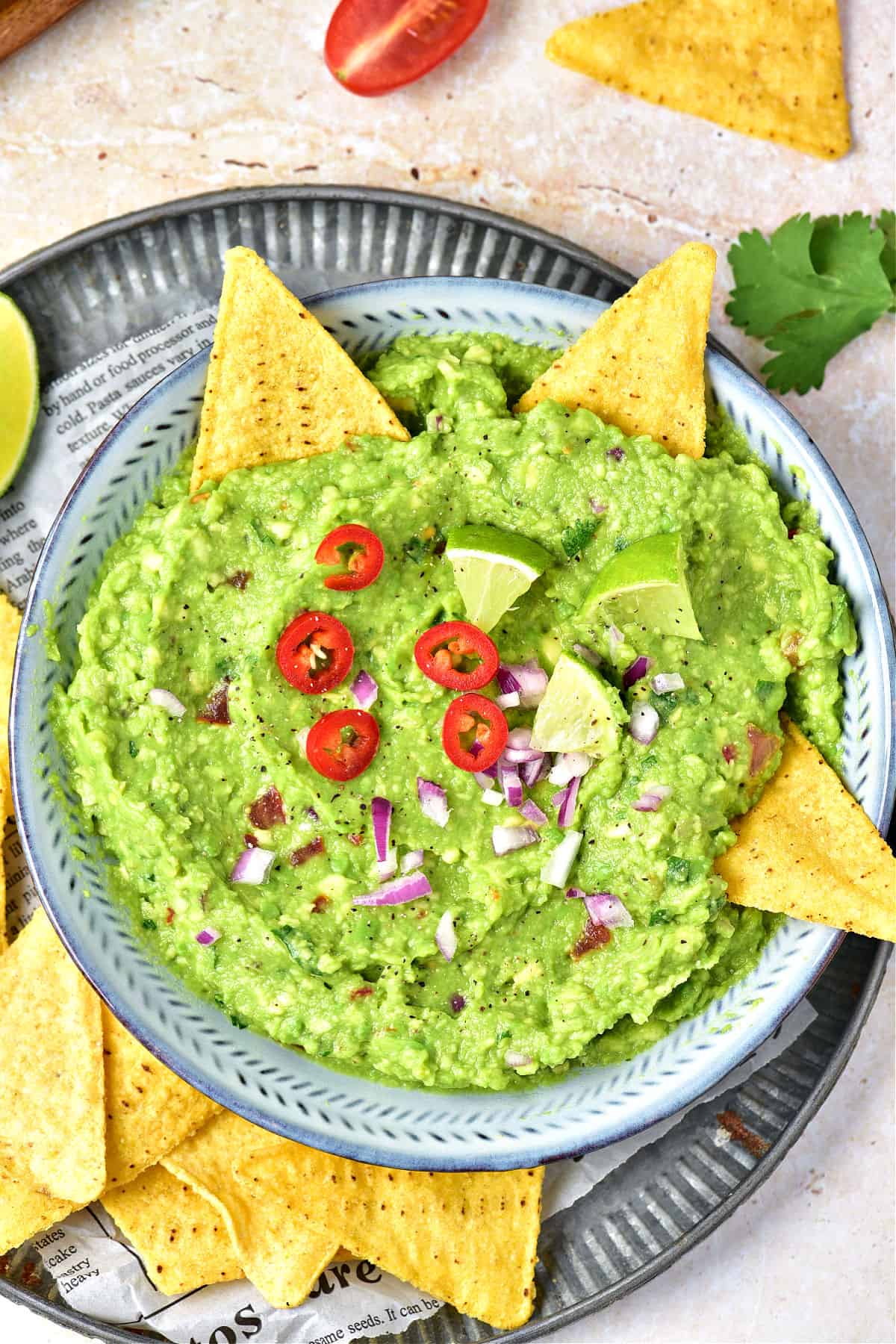 Blue bowl with guacamole, red jalapeños and tortilla chips on a metal tray. Top view.