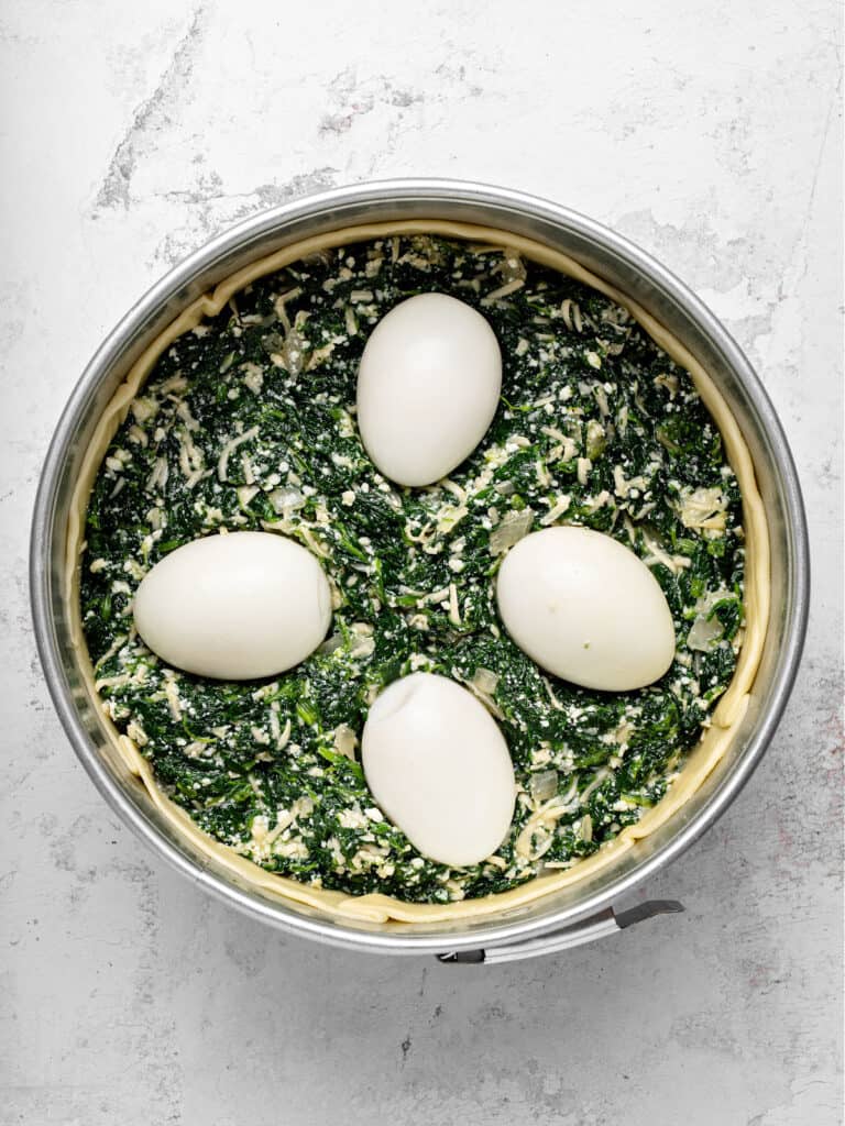 Hard-boiled eggs and spinach pie filling in a round cake springform pan. Light gray background. Top view.