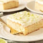 Close up lime tequila cake with cream topping on a white plate. Silver fork.