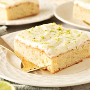 Close up lime tequila cake with cream topping on a white plate. Silver fork.