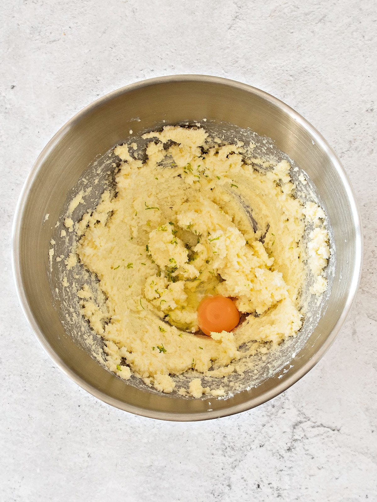 Metal bowl with butter mixture and egg. Top view, gray background.