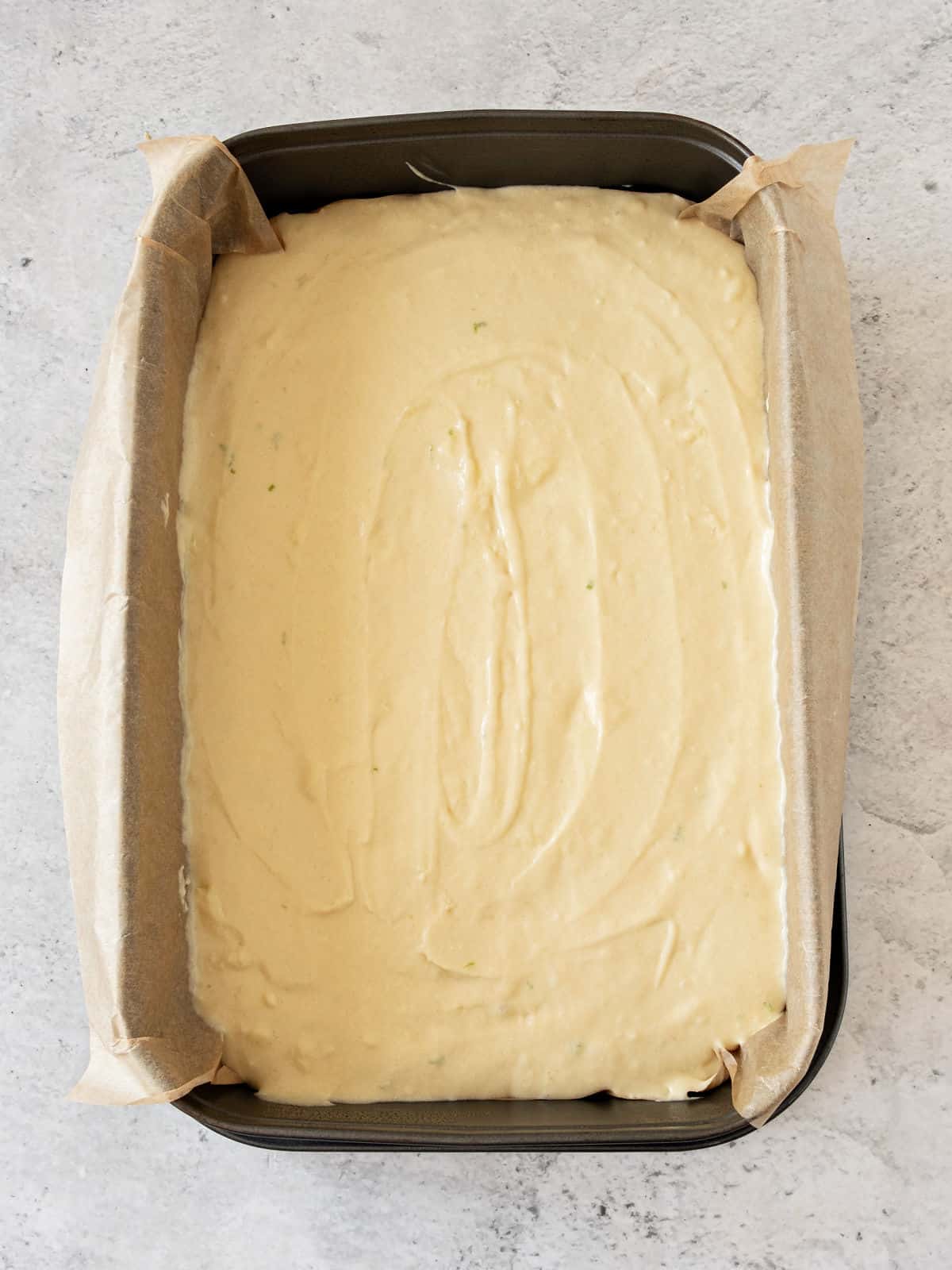 Tequila lime cake batter in a parchment lined rectangular metal pan. Gray background. Top view.