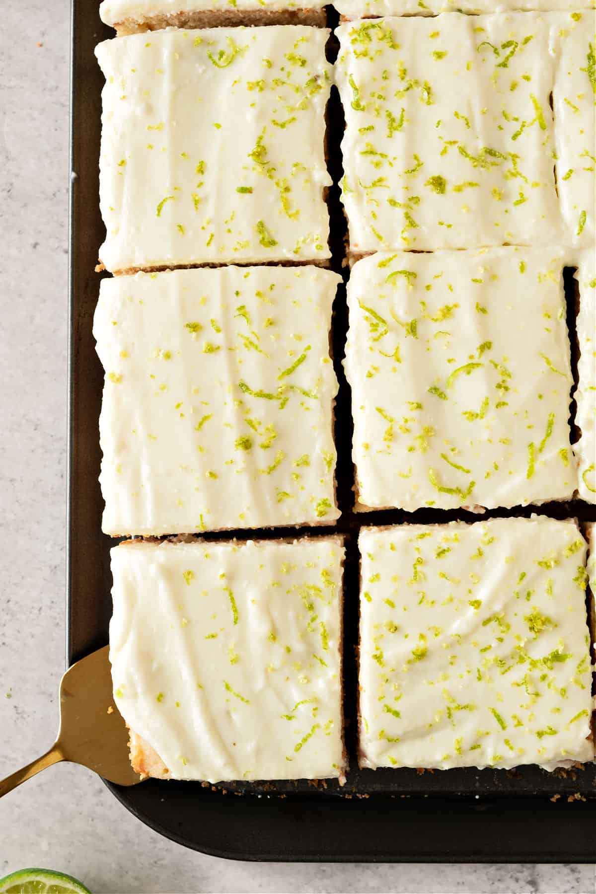 Squares of cream-topped cake with lime zest on a dark platter.
