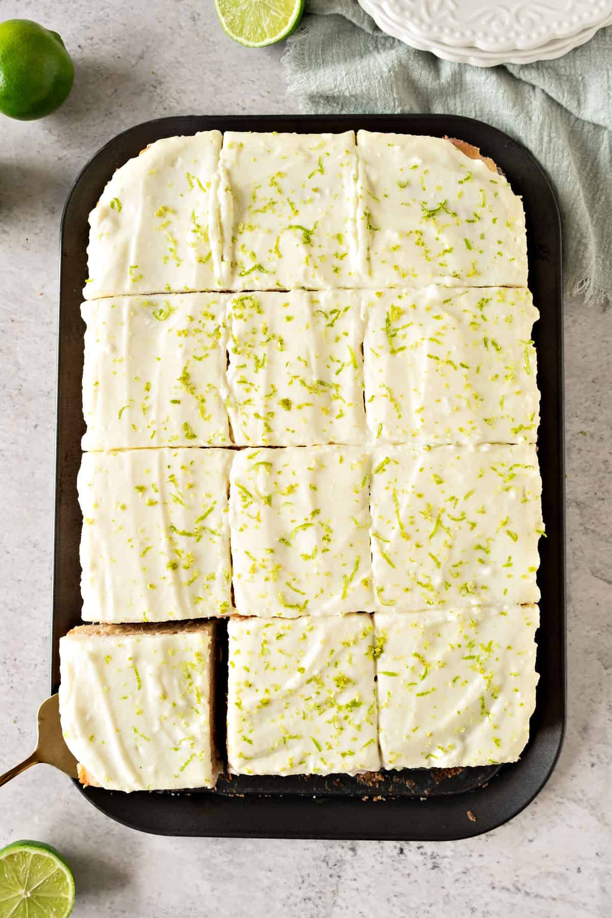 Cream and lime topped sliced rectangular cake on a dark platter. Top view.