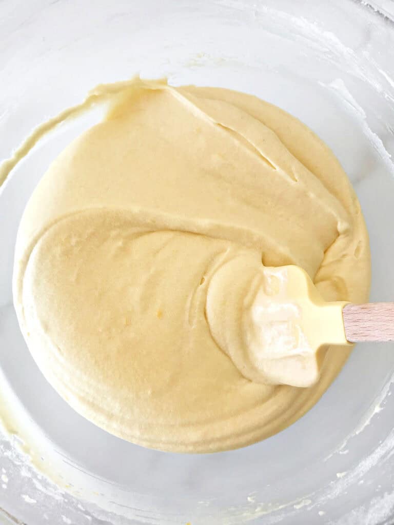 Glass bowl with vanilla cake batter and yellow wooden spatula.