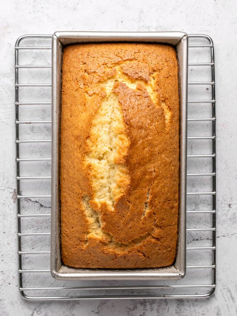 Baked lemon cake in a loaf pan on a wire rack.