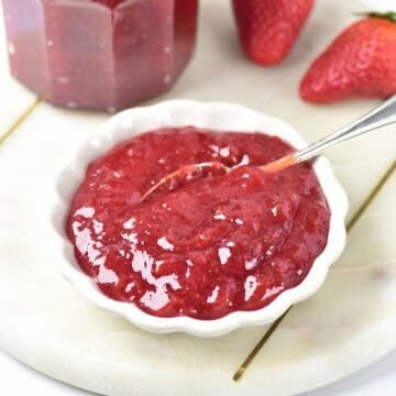 White bowl with strawberry jam. Marble board. Silver spoon and fresh strawberries.
