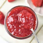 Spoon and jar of strawberry jam. White background.