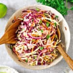 White bowl with cilantro, red and green cabbage coleslaw. Wooden serving utensils.