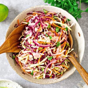 White bowl with cilantro, red and green cabbage coleslaw. Wooden serving utensils.