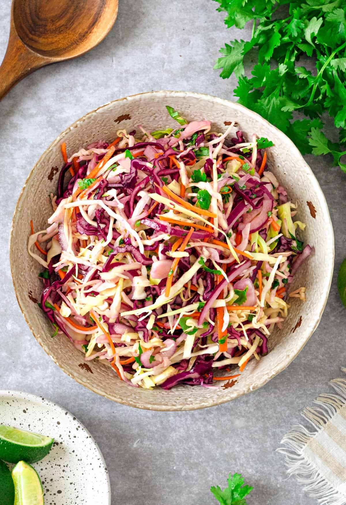 White bowl with coleslaw. Light gray background, cilantro, lime wedges.