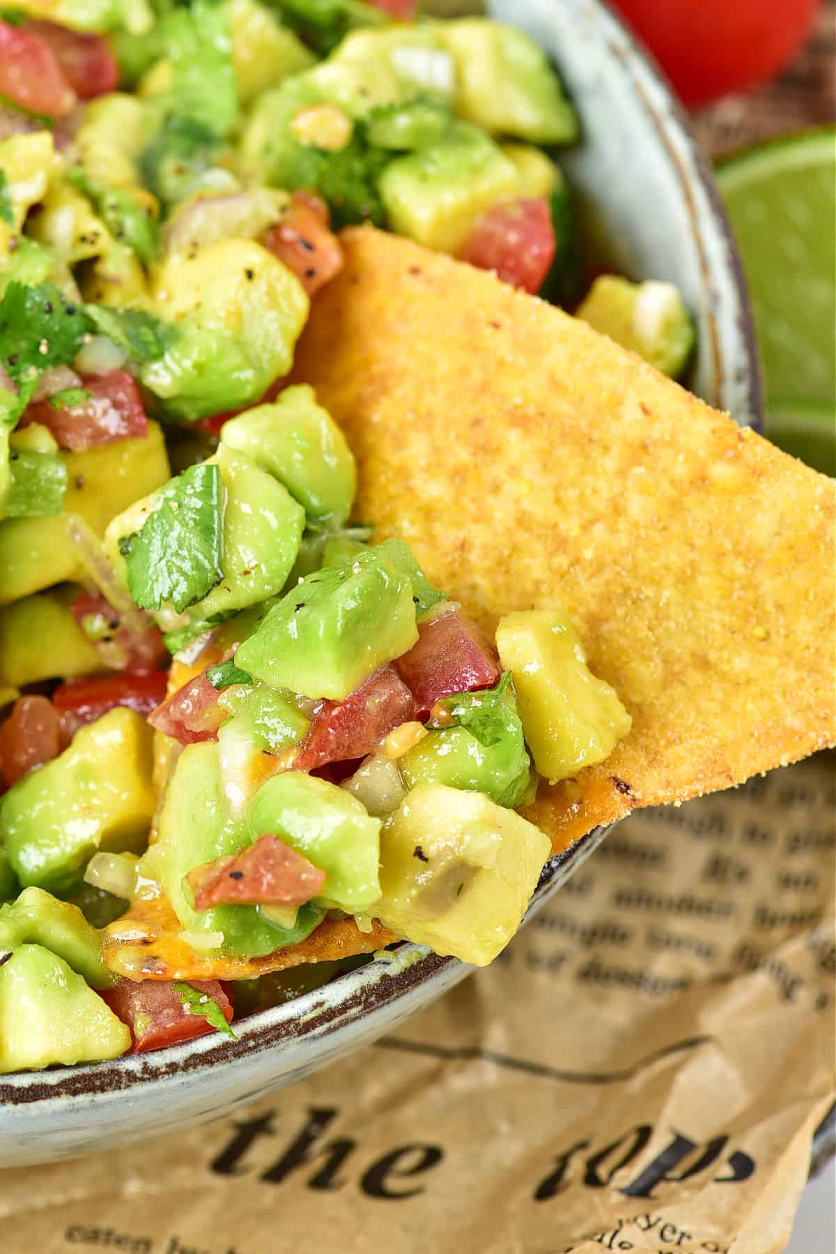 Close up tortilla chip with avocado tomato salsa in a gray bowl.