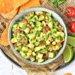 Avocado tomato salsa in a gray bowl on a newspaper. Tortilla chips, lime, tomatoes.