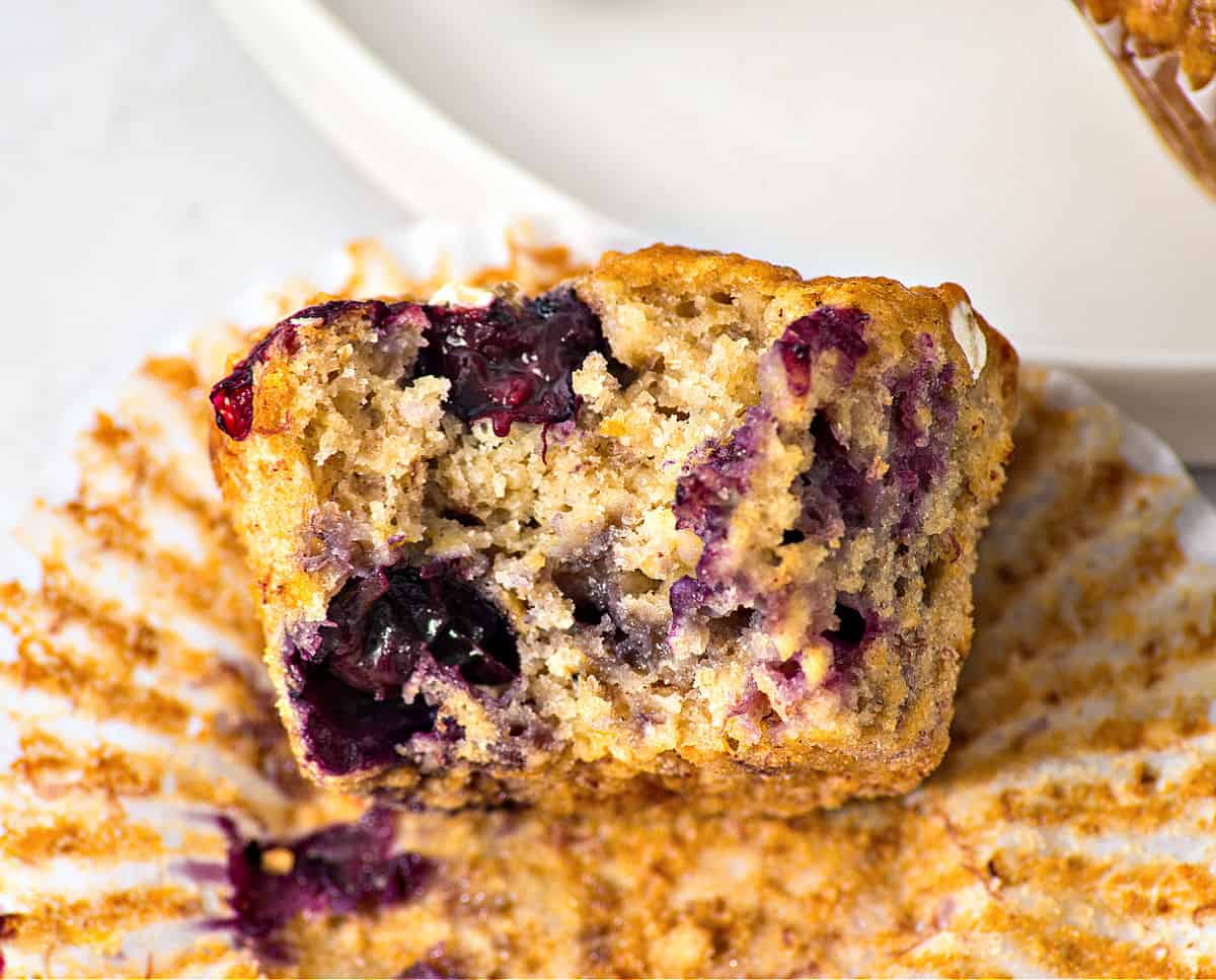 Bitten banana blueberry oat muffin on an opened paper liner.