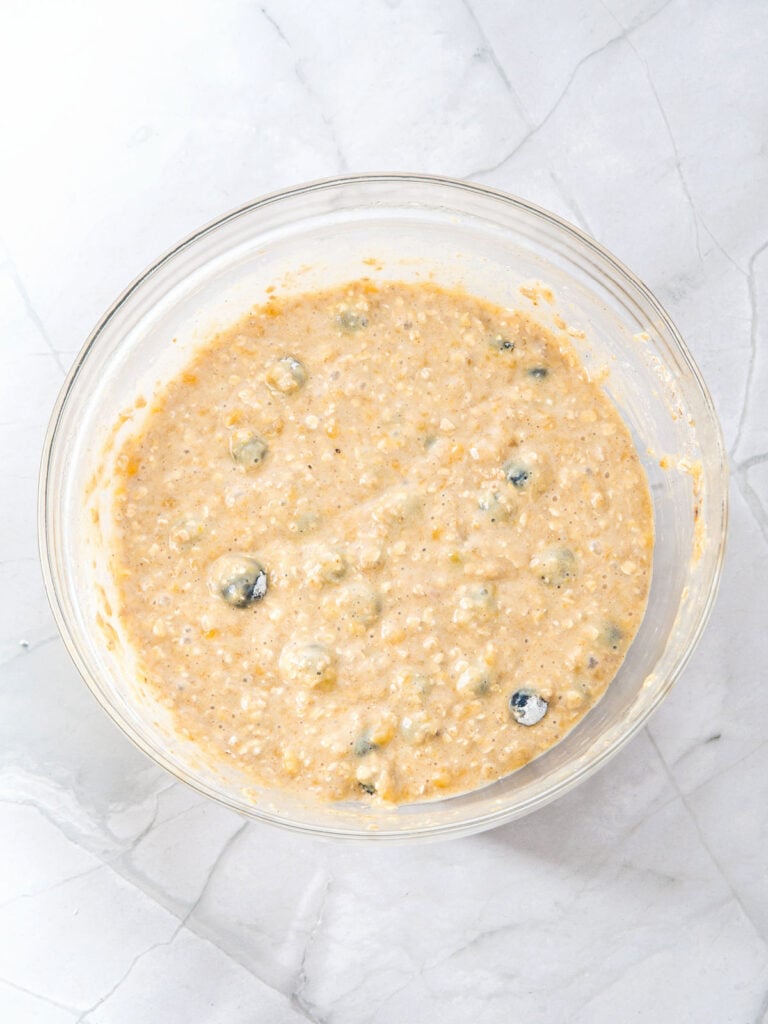 Glass bowl with blueberry banana oat muffins batter. White marbled surface, top view.