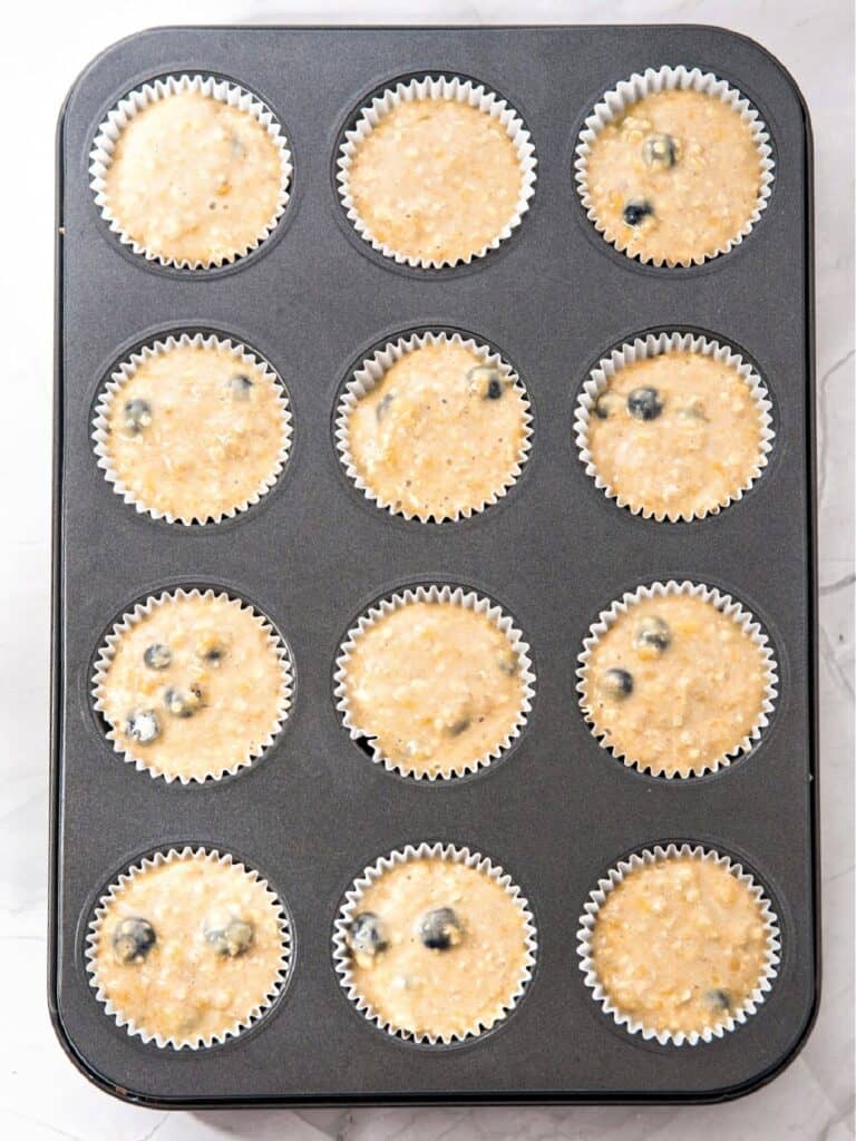 Muffin liners with banana blueberry oat muffins batter. Metal pan, top view.