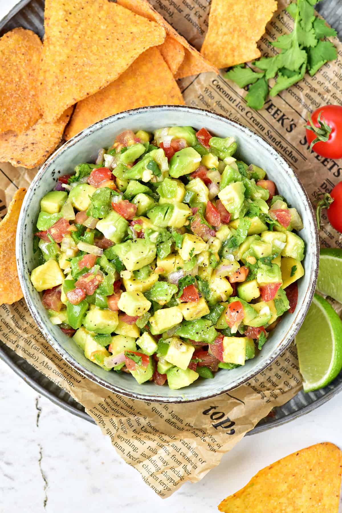 Gray bowl with avocado salsa on a newspaper with tortilla chips.