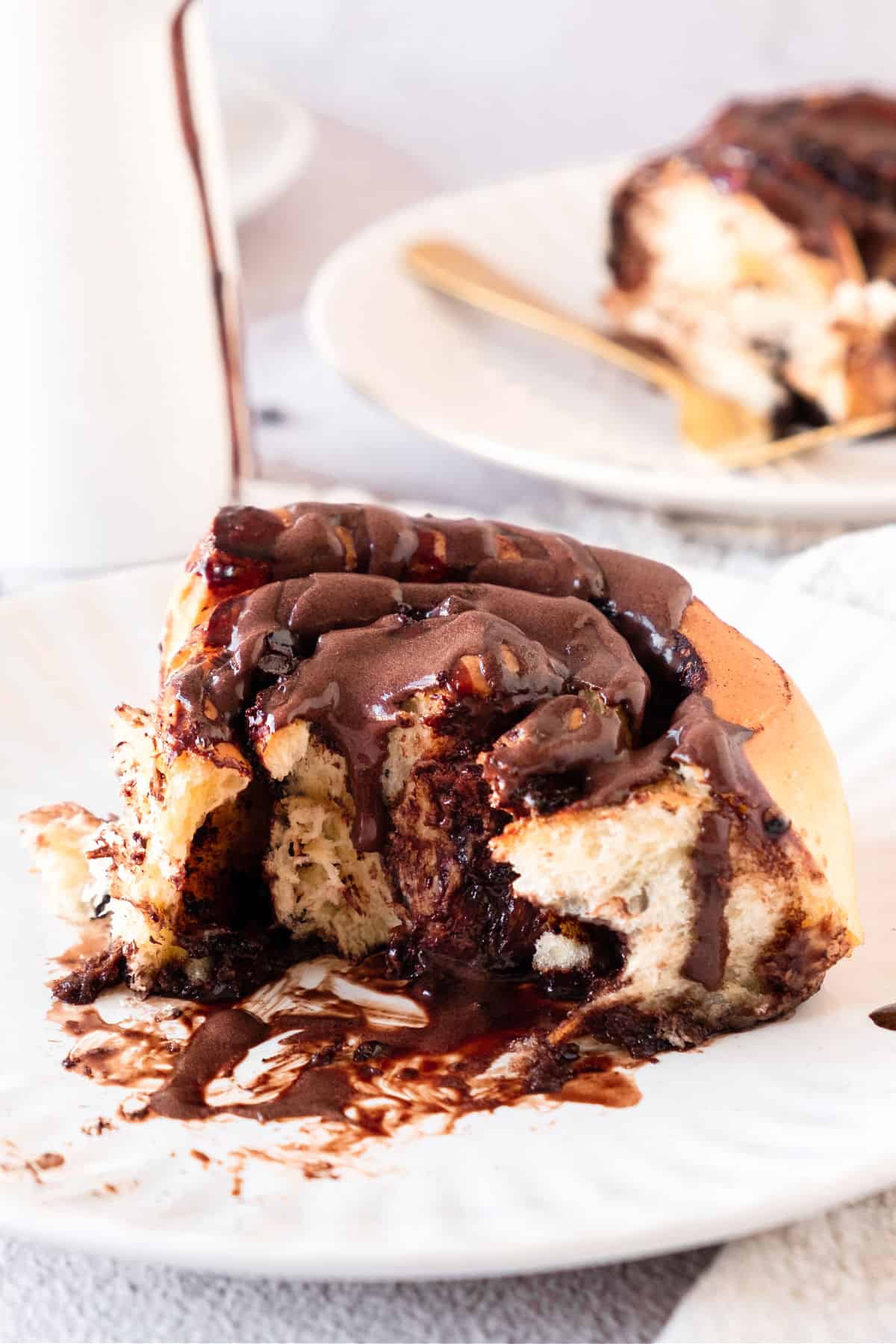 Bitten chocolate cinnamon roll on a white plate.