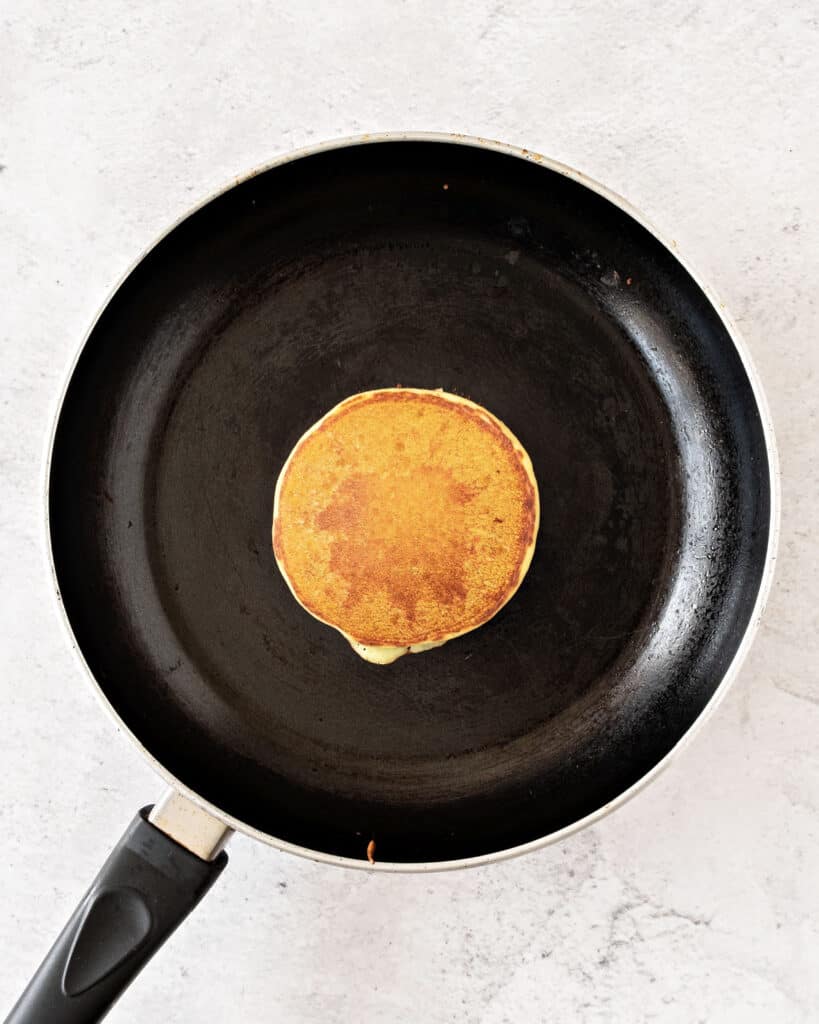 Black skillet with cooked pancake. Light gray background, top view.