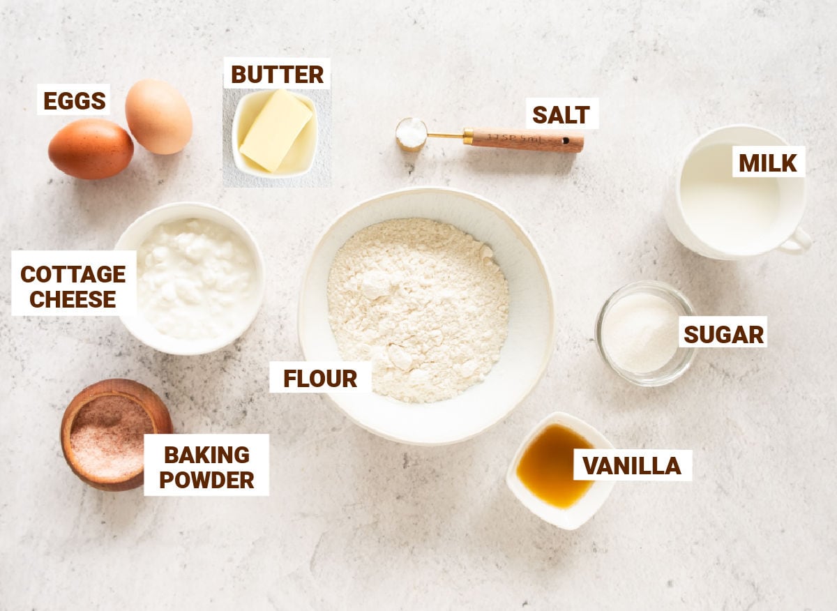 Light gray surface with white bowl containing ingredients for cottage cheese pancakes.