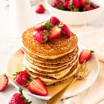 White plate with stack of cottage pancakes with strawberries and syrup. Golden fork, white background.
