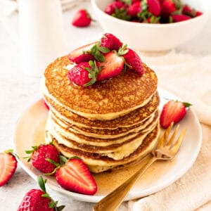 White plate with stack of cottage pancakes with strawberries and syrup. Golden fork, white background.